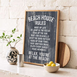 a chalkboard sign with beach house rules, accompanied by a wooden board, a vase with a plant, and a bowl of lemons, all placed on a white countertop.