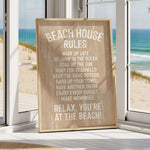 A wooden sign with beach rules posted in a room with a view of the ocean through a window.
