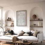 a cozy living room with a white sofa, a wooden coffee table, and a framed sign that reads "LAKESHORE RULES" above the sofa. The room has arched doorways, and there are shelves displaying decorative items and a vase on the wall.