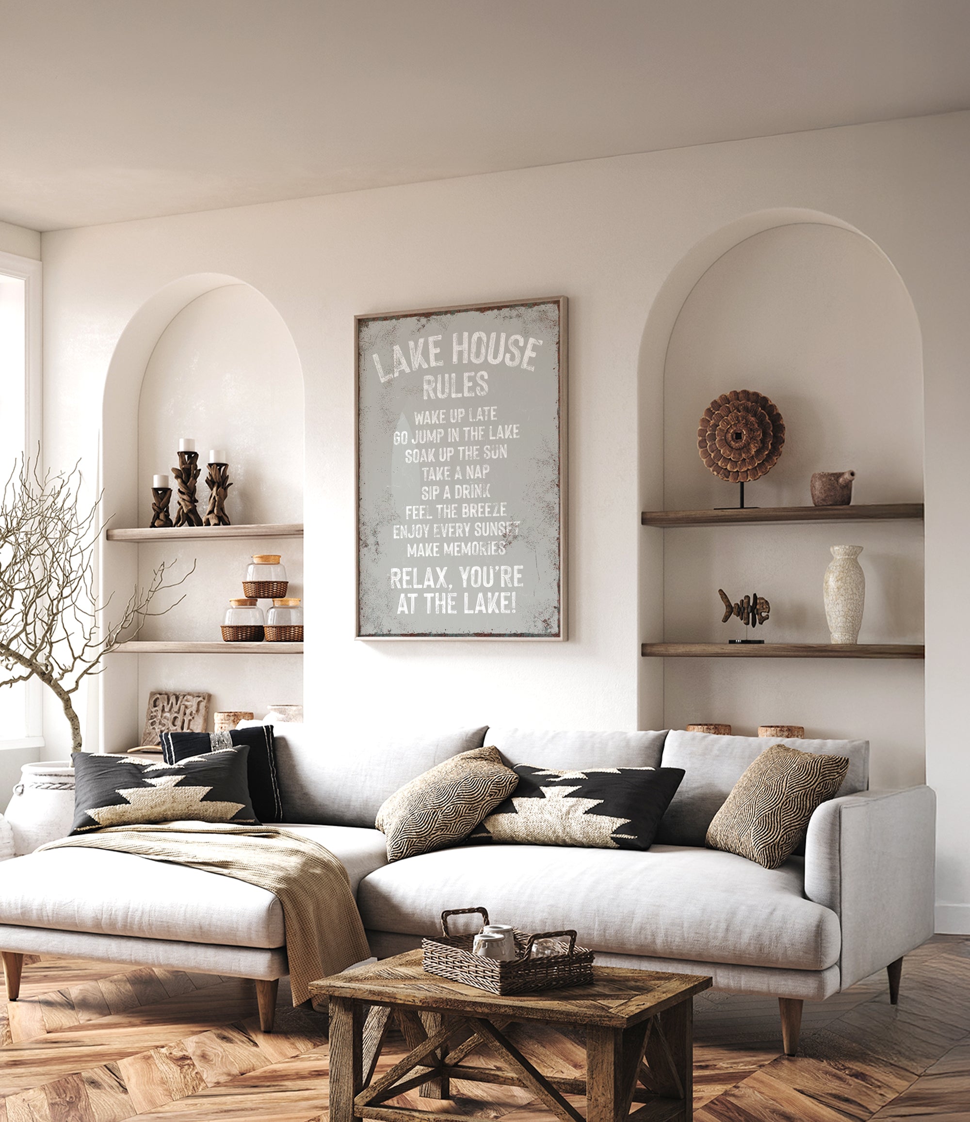a cozy living room with a white sofa, a wooden coffee table, and a framed sign that reads "LAKESHORE RULES" above the sofa. The room has arched doorways, and there are shelves displaying decorative items and a vase on the wall.