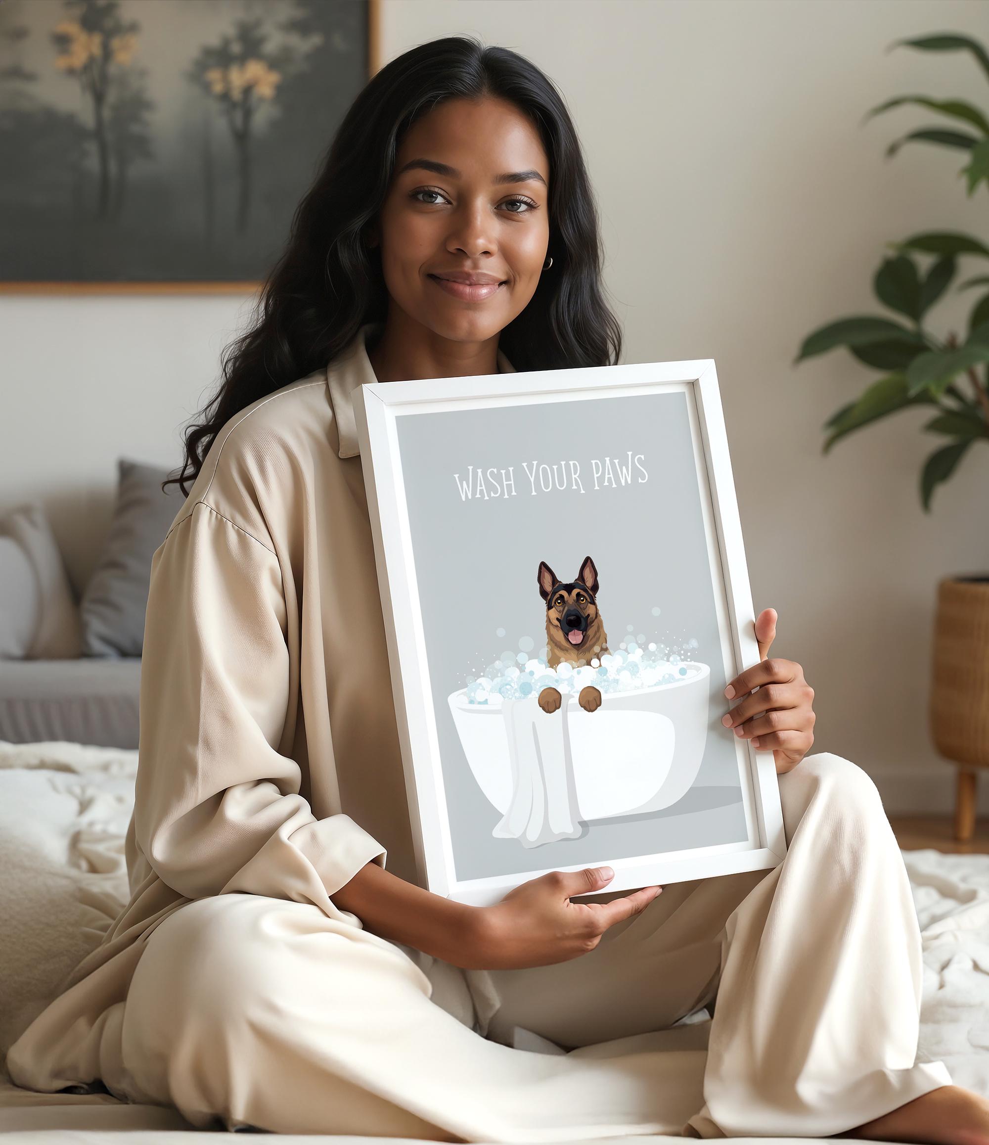 A woman in a beige outfit is sitting on a bed and holding up a framed poster with a dog in a bathtub.