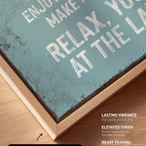 a close-up view of a textured, weathered canvas print with a wooden frame. The text on the canvas is in white and reads "Enjoy life, make memories, relax at the lake".