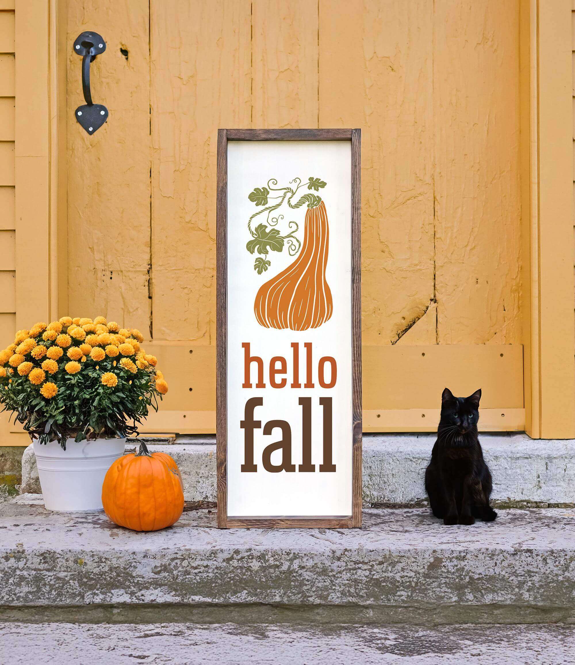 a black cat sitting next to a sign that says hello fall