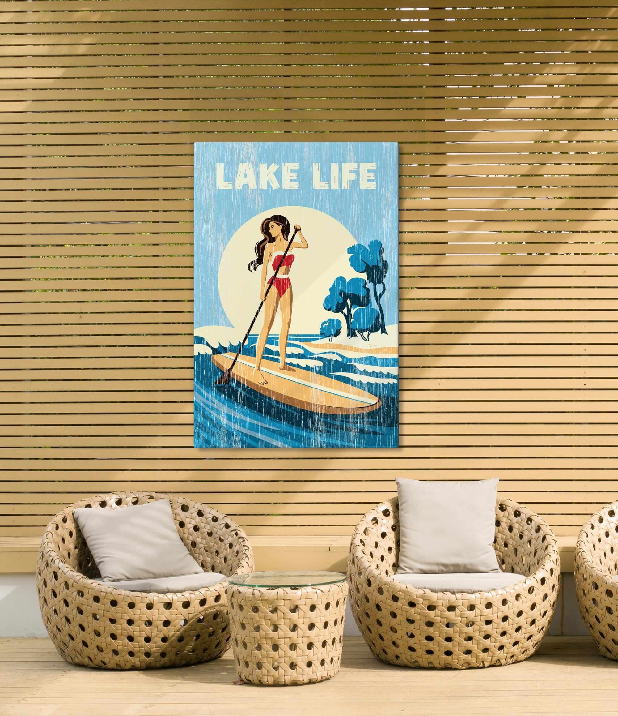 a woman paddleboarding on a lake, with a sign above her that says "LAKELIFE". The scene is set against a wooden wall with wicker furniture, including two chairs and a small table.