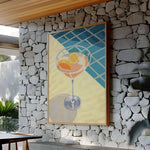 a large painting of a cocktail glass with orange slices, hanging on a stone wall.