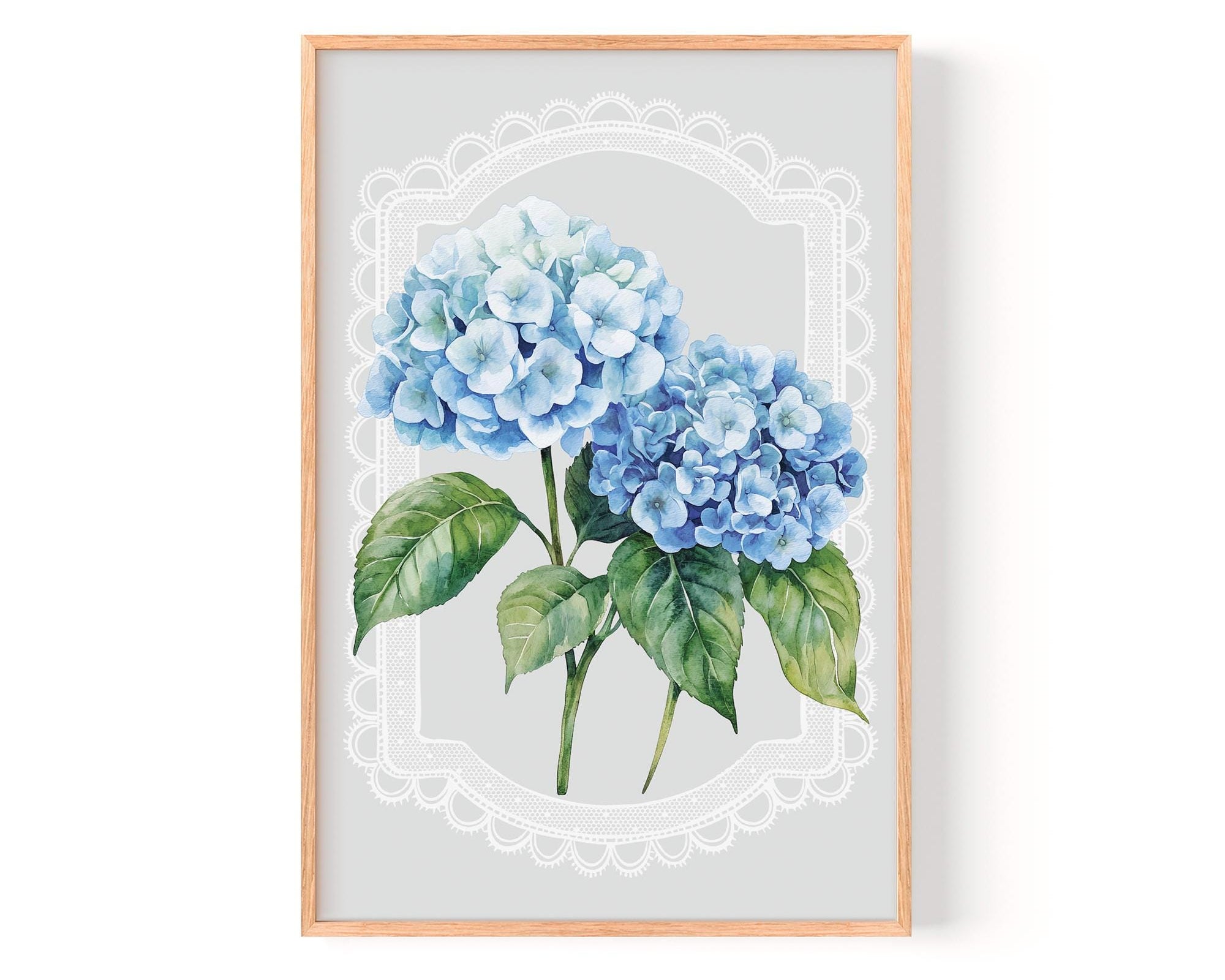 A framed print of two blue hydrangea flowers with green leaves, set against a light gray background with a white lace-like border.