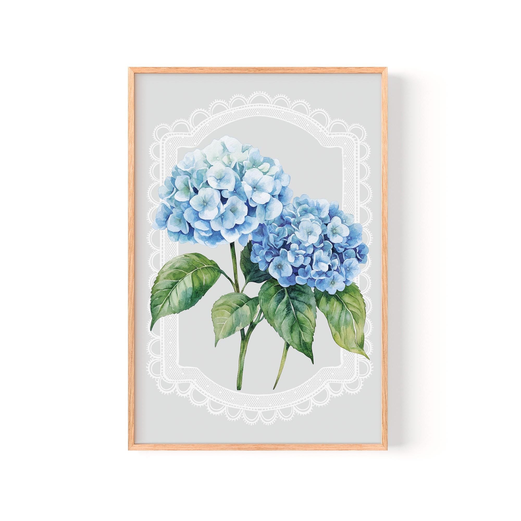 A framed print of two blue hydrangea flowers with green leaves, set against a light gray background with a white lace-like border.
