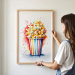 A woman is holding up a framed painting of a colorful bucket of popcorn on a wall.