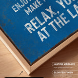 The image is a close-up of a blue canvas print with white text, placed on a wooden surface.