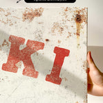 a close-up view of a white canvas print with a red letter "K" and some rust stains on it.