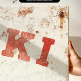 a close-up view of a white canvas print with a red letter "K" and some rust stains on it.