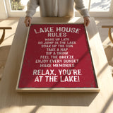 A person is holding up a framed sign with a red background and white text, which appears to be a list of rules or instructions for a lake house.