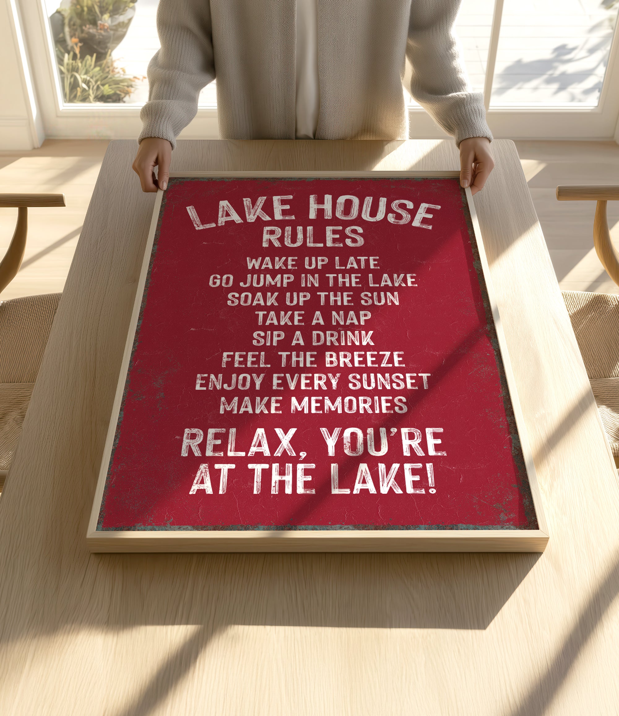 A person is holding up a framed sign with a red background and white text, which appears to be a list of rules or instructions for a lake house.