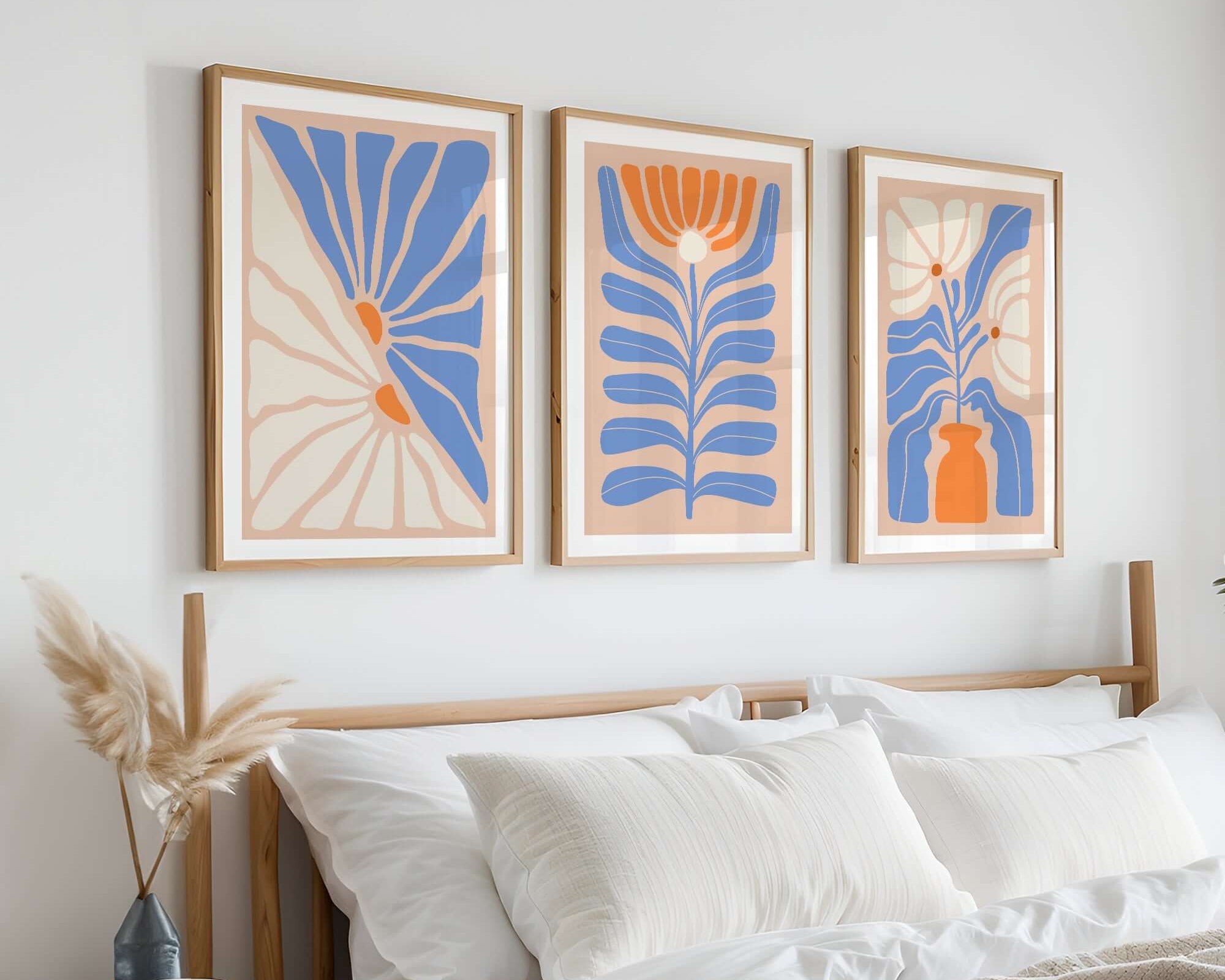 A cozy bed with white linens is complemented by the Flower Blocks Triptych | Set of Three Prints | 010, a collection of abstract blue and orange wall art hanging above the headboard.