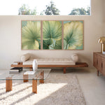 a modern living room with a large window, a glass coffee table, a sofa, and a rug. The room has a minimalist and clean design, with a focus on natural elements such as the large leaf-like artwork on the wall.