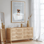 a wooden dresser with a framed poster of a dog sitting in a bathtub, accompanied by the text "WASH YOUR PAWS". The dresser is situated in a room with a mirror and a window, creating a cozy and stylish atmosphere.