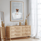 a wooden dresser with a framed poster of a dog sitting in a bathtub, accompanied by the text "WASH YOUR PAWS". The dresser is situated in a room with a mirror and a window, creating a cozy and stylish atmosphere.
