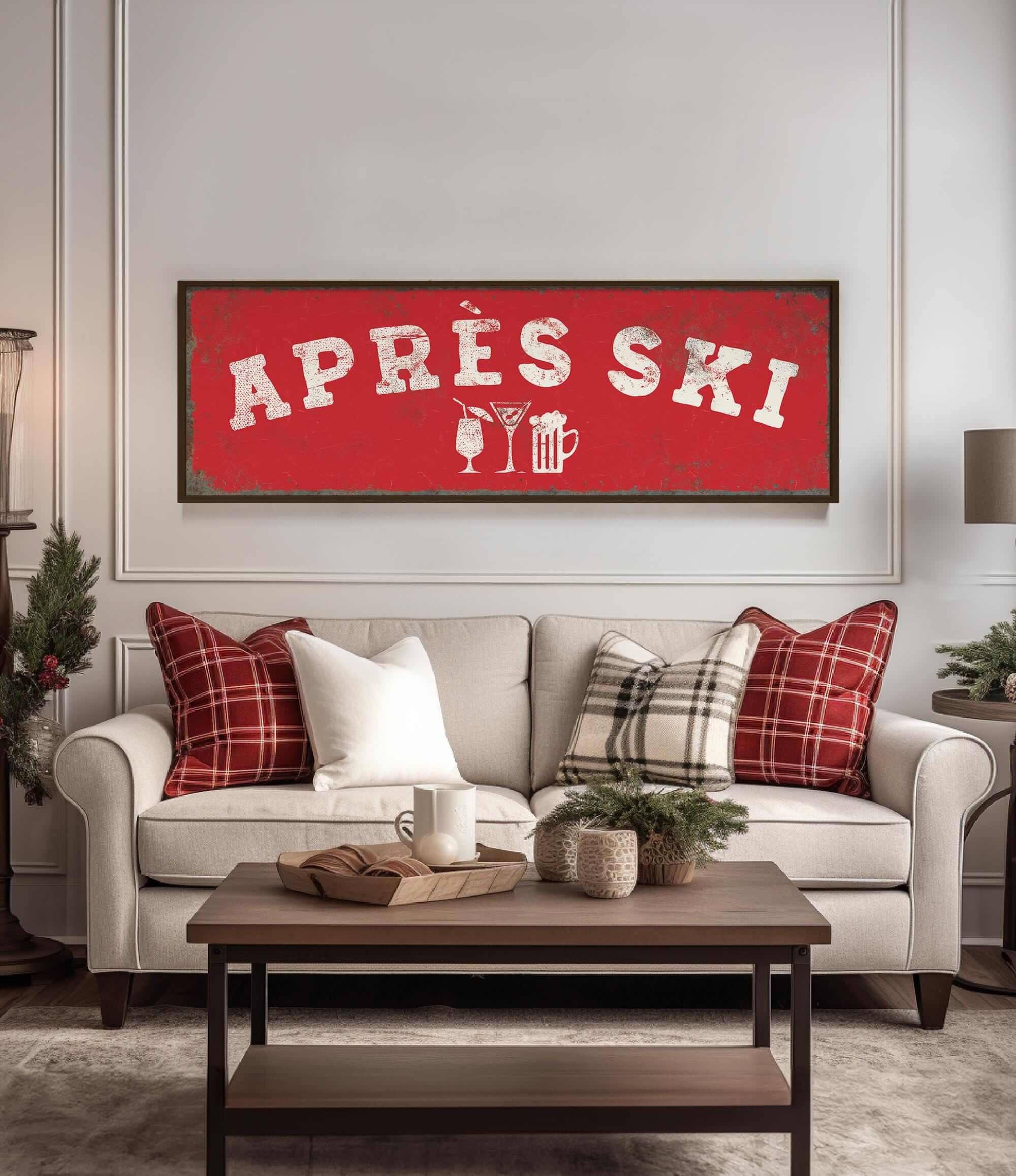 a cozy living room with a large red sign that says "APRÈS SKI" in bold white letters. The sign is mounted on a white wall above a beige sofa with red and white plaid throw pillows. In front of the sofa, there is a wooden coffee table with a tray and a mug. The room also includes a potted plant, a lamp, and a vase, creating a warm and inviting atmosphere.