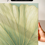 a close-up view of a leaf with intricate patterns and textures, held up against a white background.