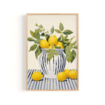 A framed painting depicting a vase filled with lemons and green leaves, placed on a striped surface.