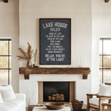 a cozy living room with a fireplace, a wooden mantel, and a framed sign that reads "Lake House Rules" above the fireplace.
