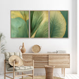 a modern living room with a wooden dresser, a woven basket, and a woven chair. Above the dresser, there are three framed prints of green leaves on a white wall, creating a cohesive and visually appealing design.