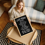 A woman is sitting on a couch and holding up a blackboard sign with white text.
