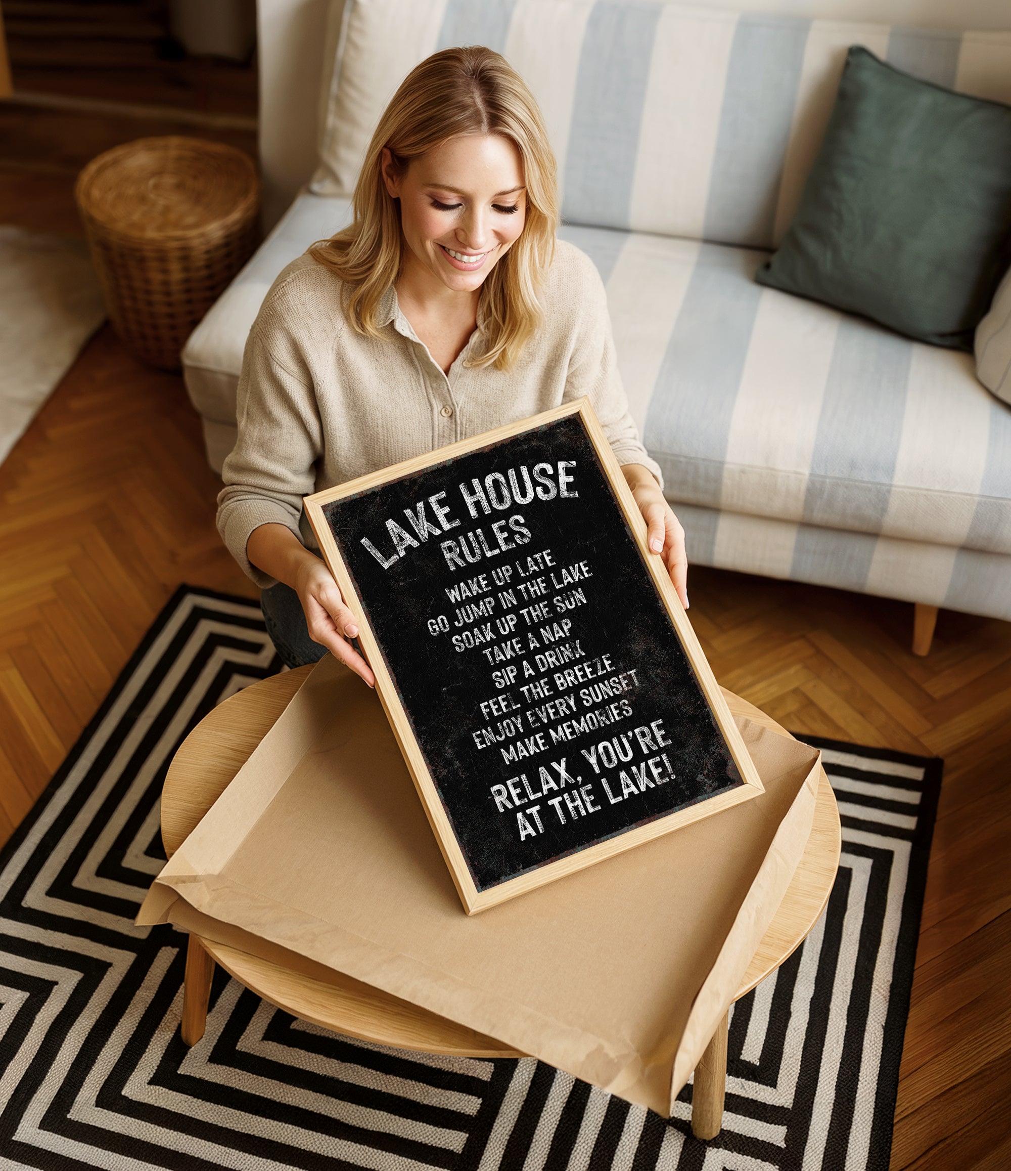 A woman is sitting on a couch and holding up a blackboard sign with white text.
