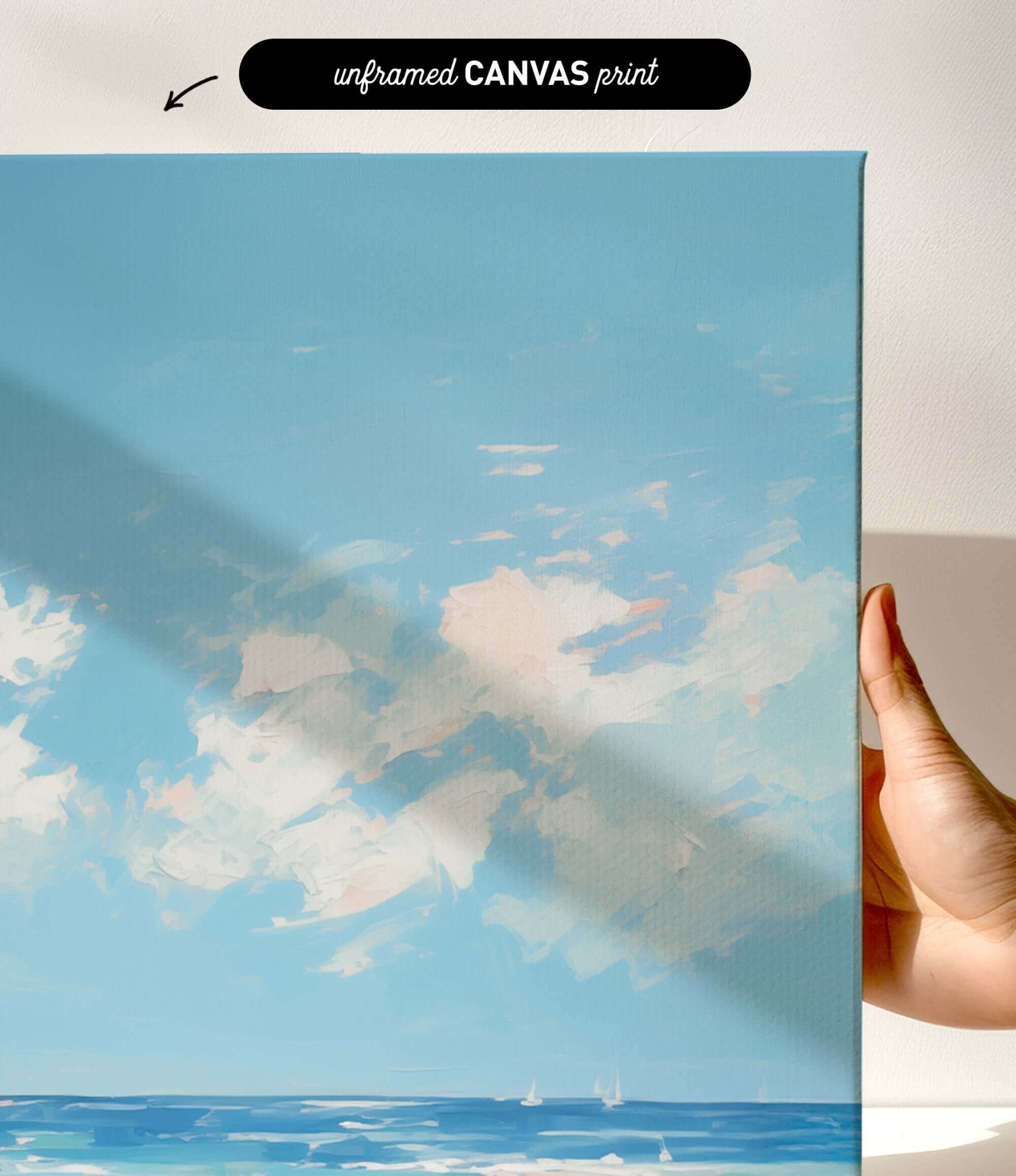 a hand holding a framed canvas print of a serene landscape depicting a blue sky with fluffy white clouds and a body of water with sailboats.