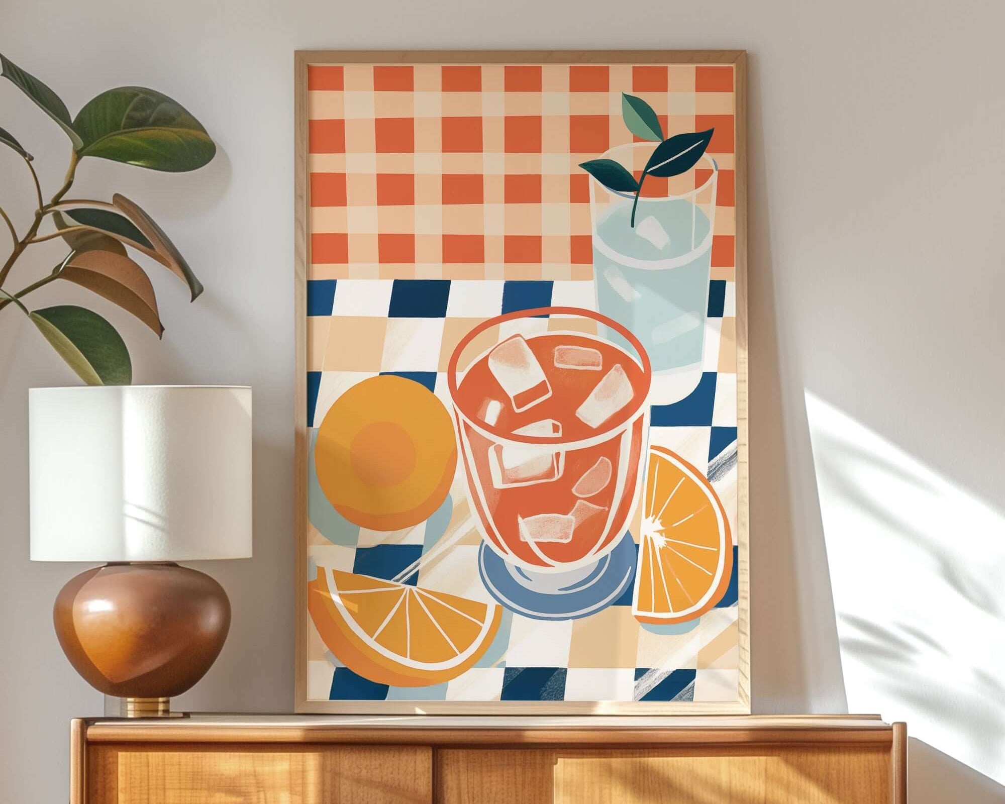 a wooden cabinet with a lamp on top, and a framed artwork depicting a glass of orange juice and slices of orange on a checkered tablecloth.