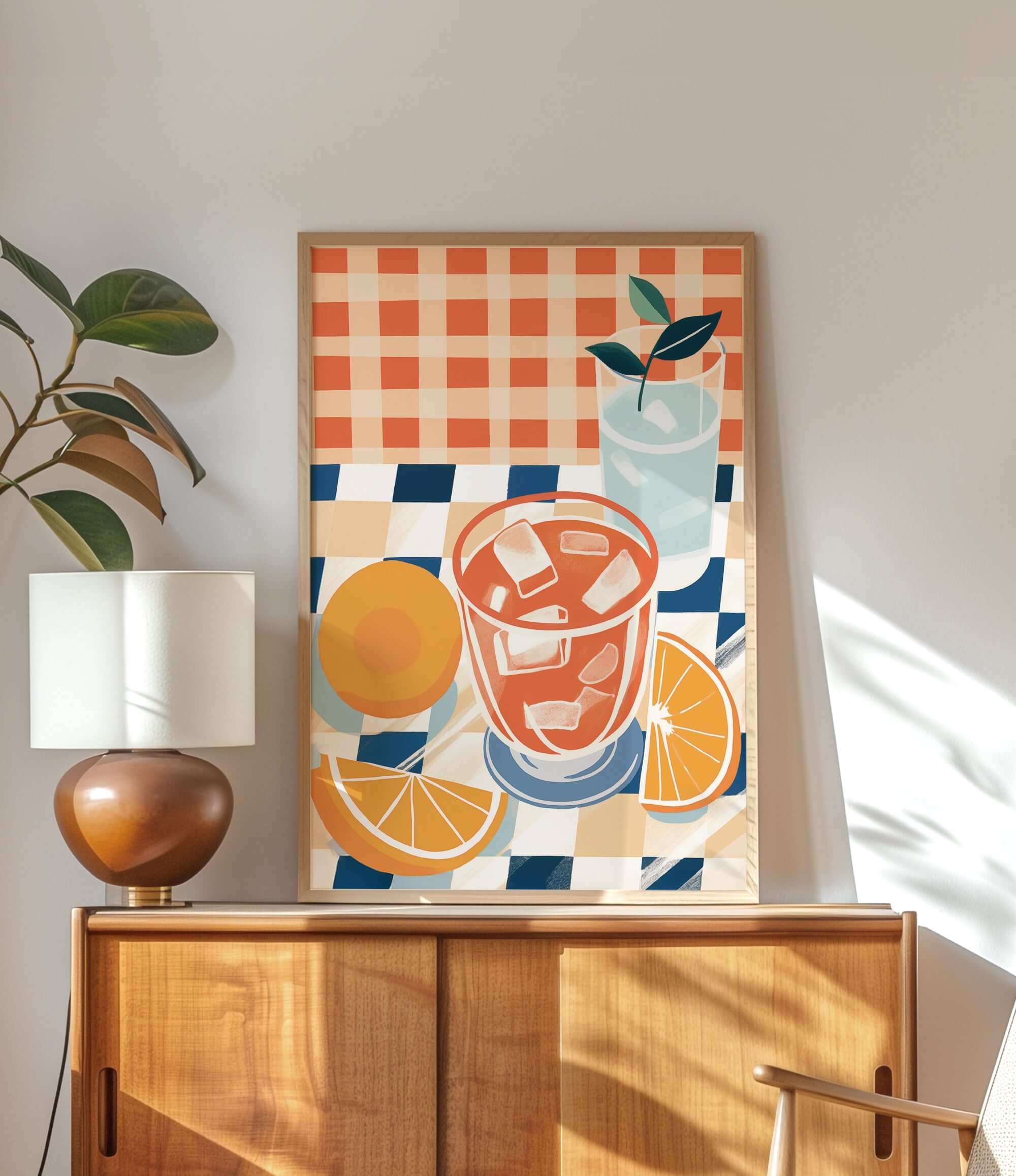 a wooden cabinet with a lamp on top, and a framed artwork depicting a glass of orange juice and slices of orange on a checkered tablecloth.