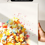 The image is a watercolor painting of a pile of popcorn, with splashes of color and a hand holding the canvas.