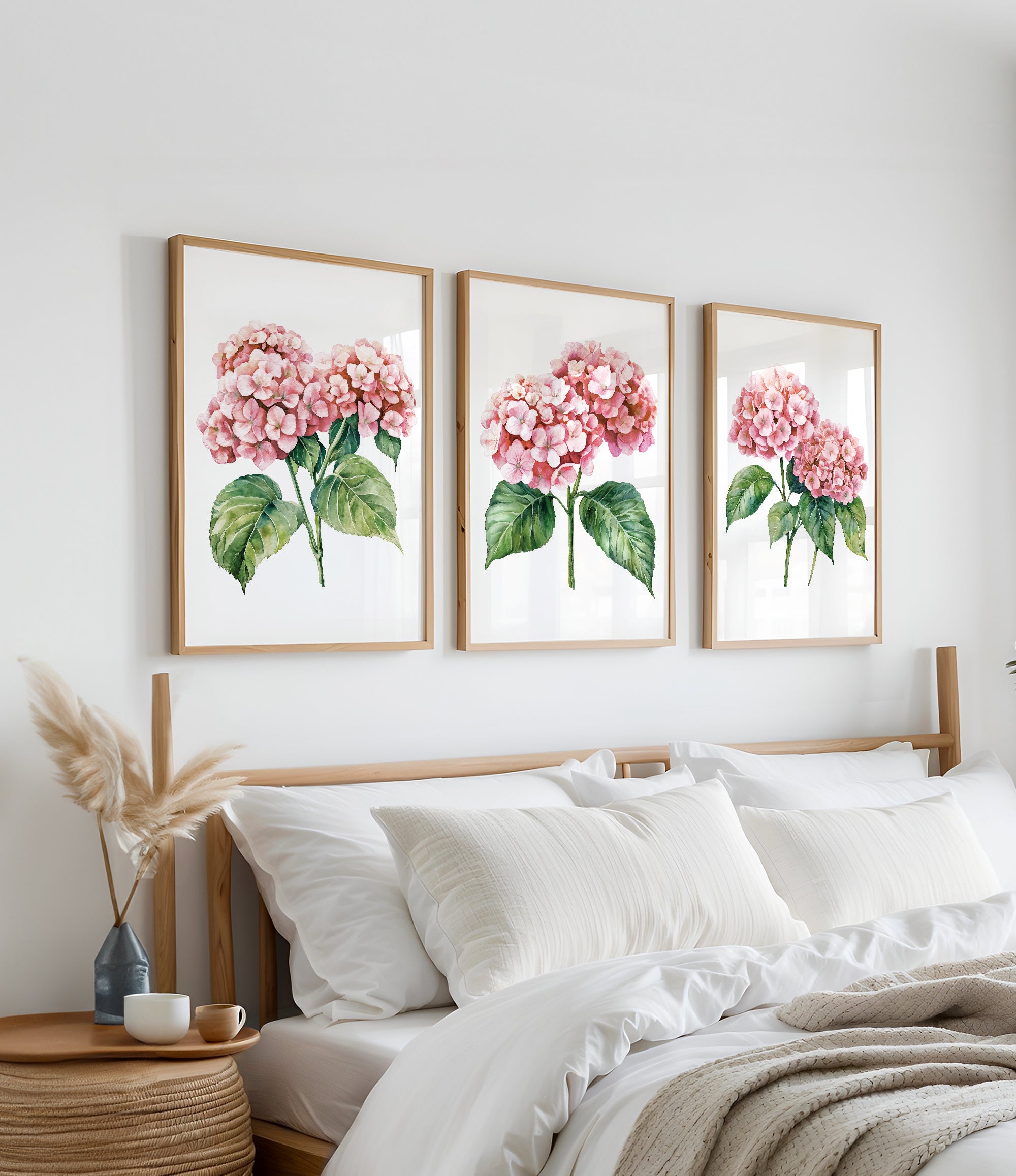 a bedroom with a bed, white pillows, and a wooden headboard. Above the bed, there are three framed watercolor paintings of pink hydrangeas hanging on the wall.