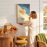 A woman hangs a framed artwork on a white wall in a cozy kitchen setting.