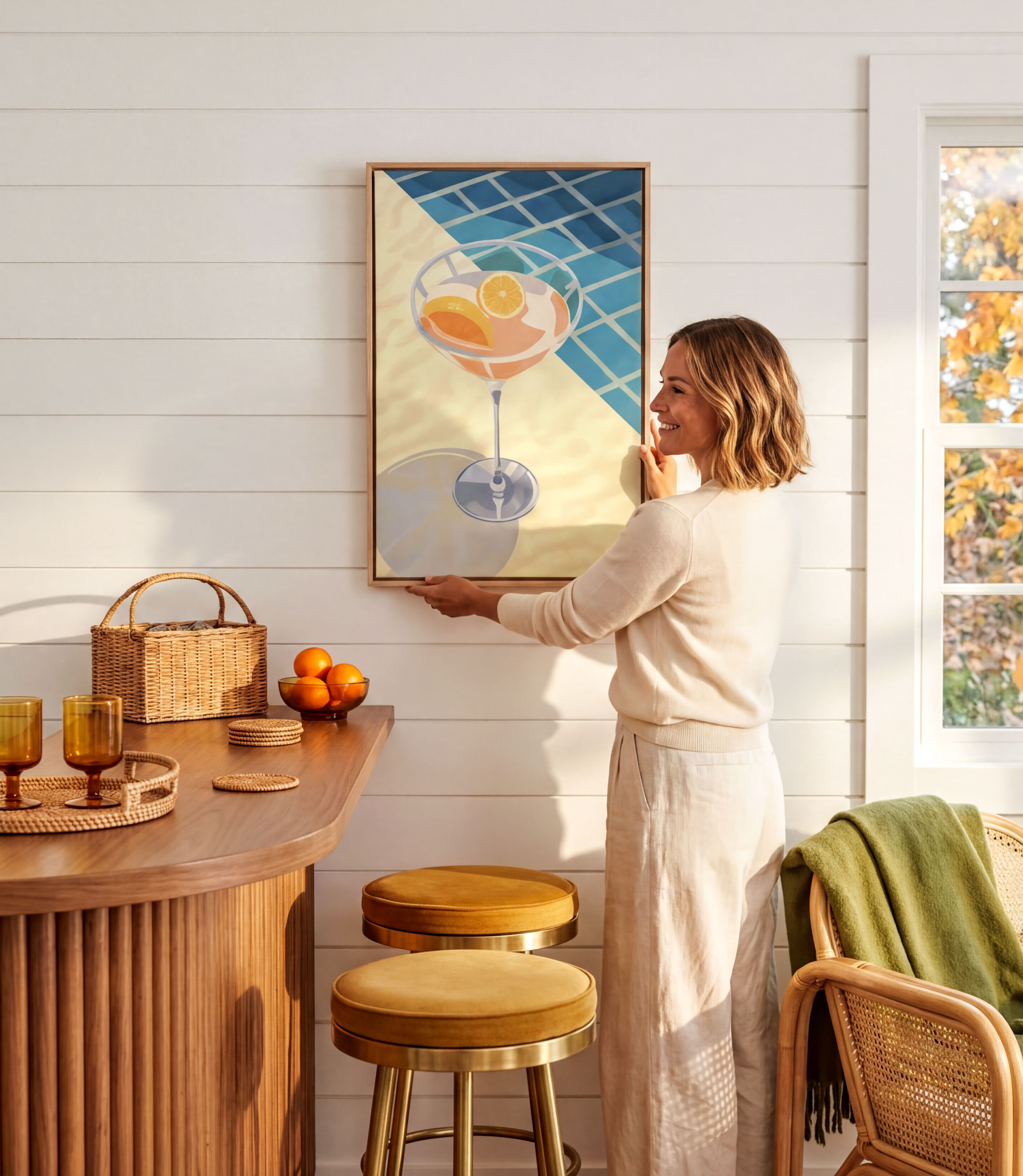 A woman hangs a framed artwork on a white wall in a cozy kitchen setting.