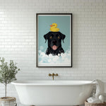 A framed illustration of a black dog with a yellow rubber duck on its head, sitting in a bathtub filled with bubbles, is displayed on a white tiled wall above a white freestanding bathtub.