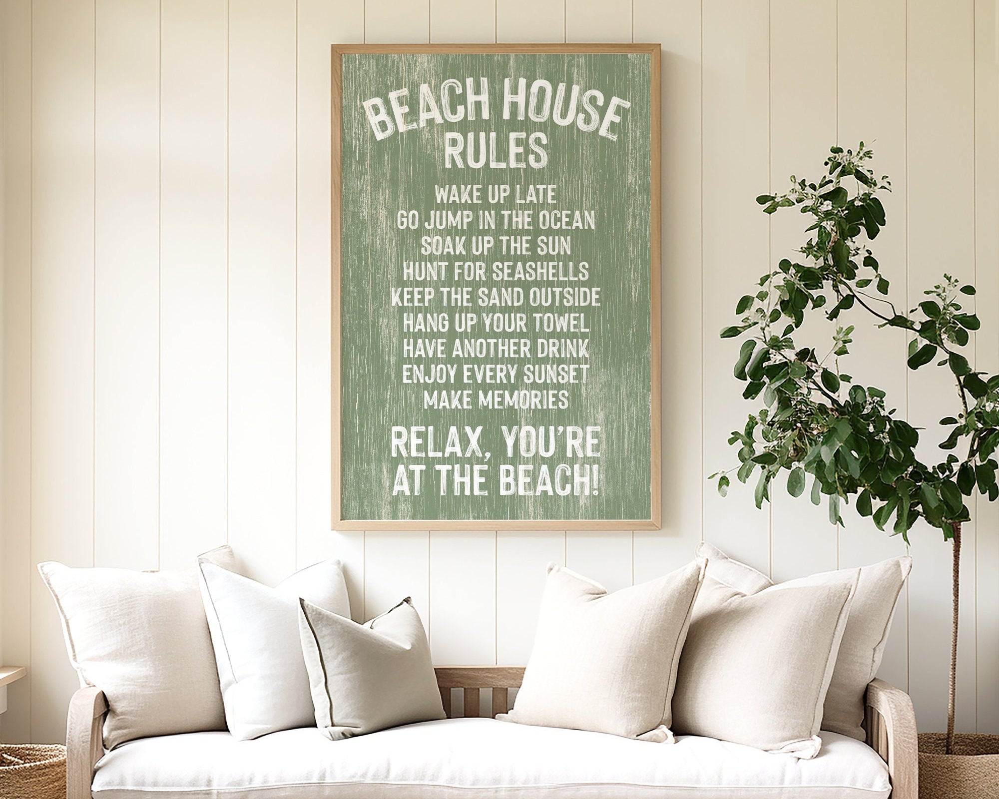 Cozy couch with white pillows in a beach house, topped by the Beach House Rules Sign in painted wood with seagrass, adding the perfect coastal wall art above.