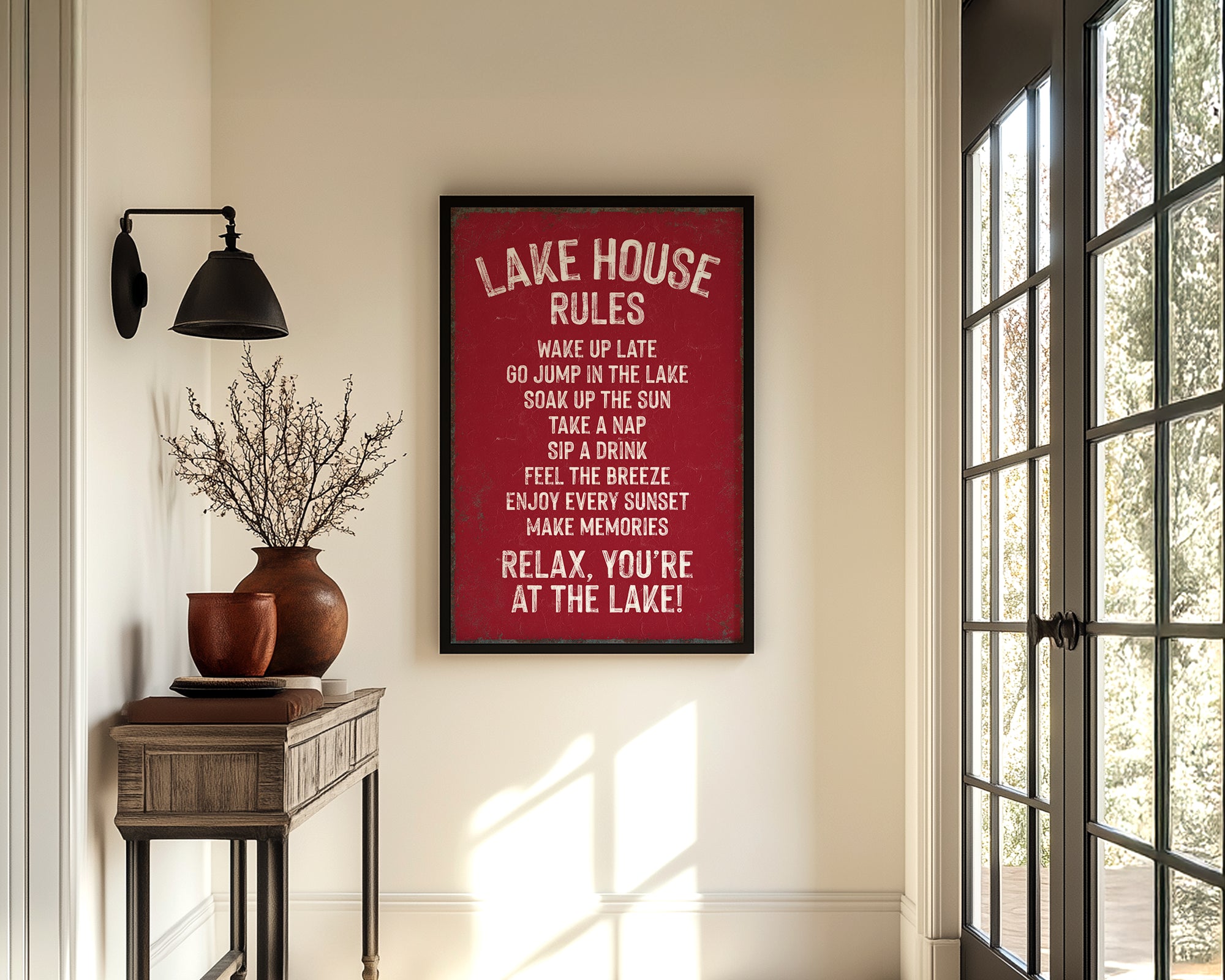 a hallway with a framed sign that reads "LAKESHORE RULES" hanging on the wall. The hallway has a wooden table with a vase of flowers, a rug, and a window with a view of trees outside.