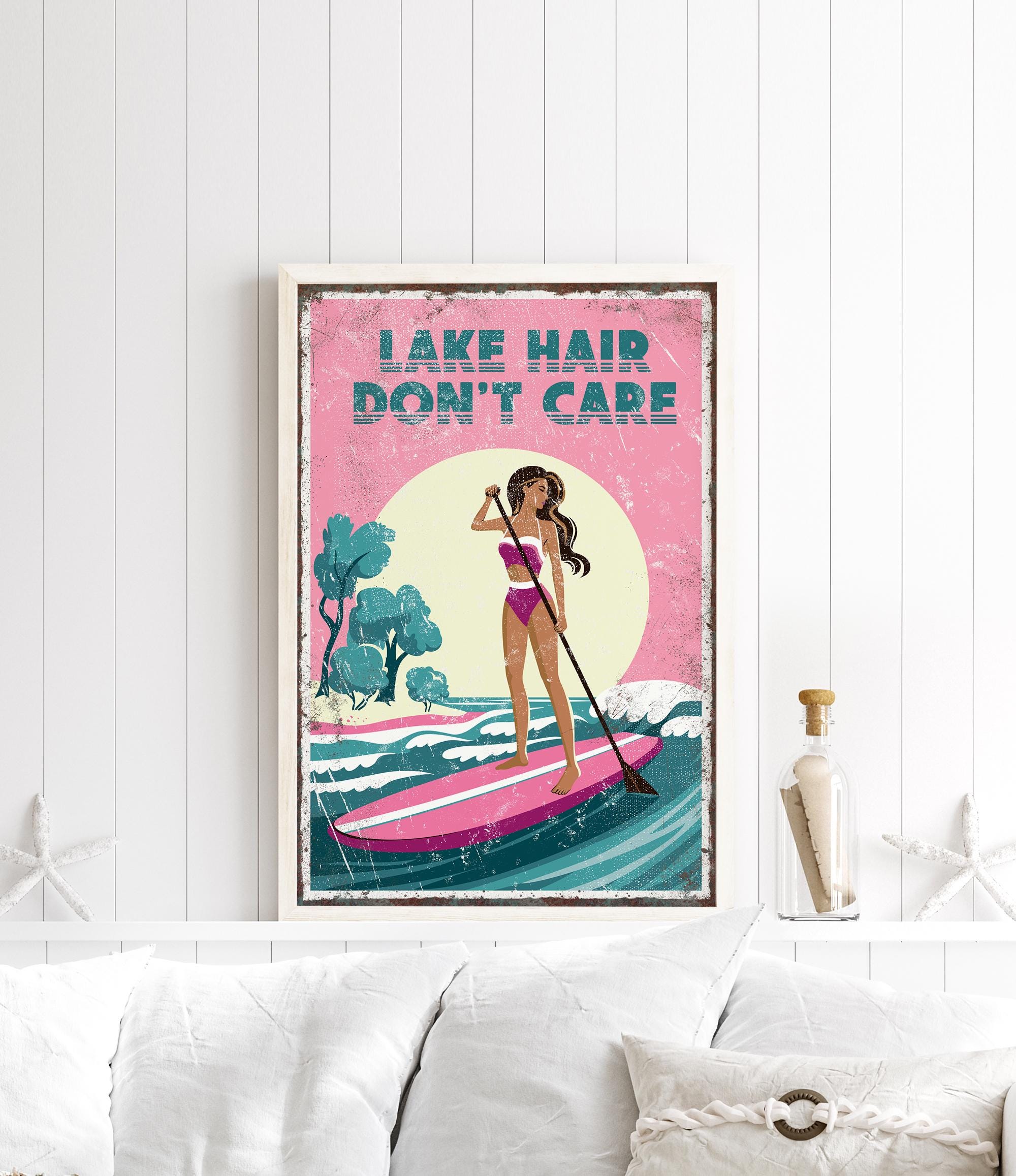 a framed poster with a woman paddleboarding on a lake, with the text "LAKESHAIR DON'T CARE" written on it.