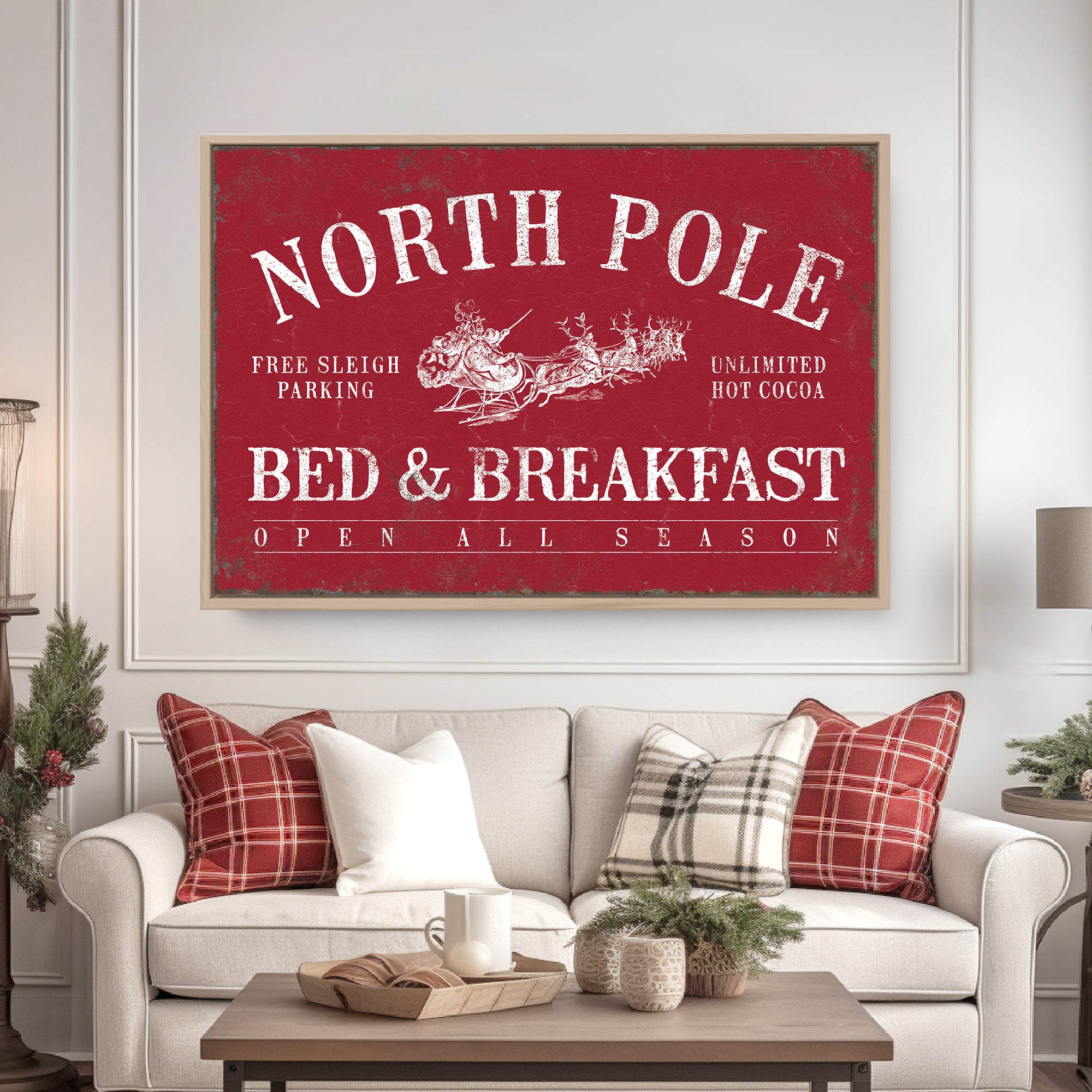 Red "North Pole Bed & Breakfast" sign above a sofa with plaid pillows in a cozy, festive living room.