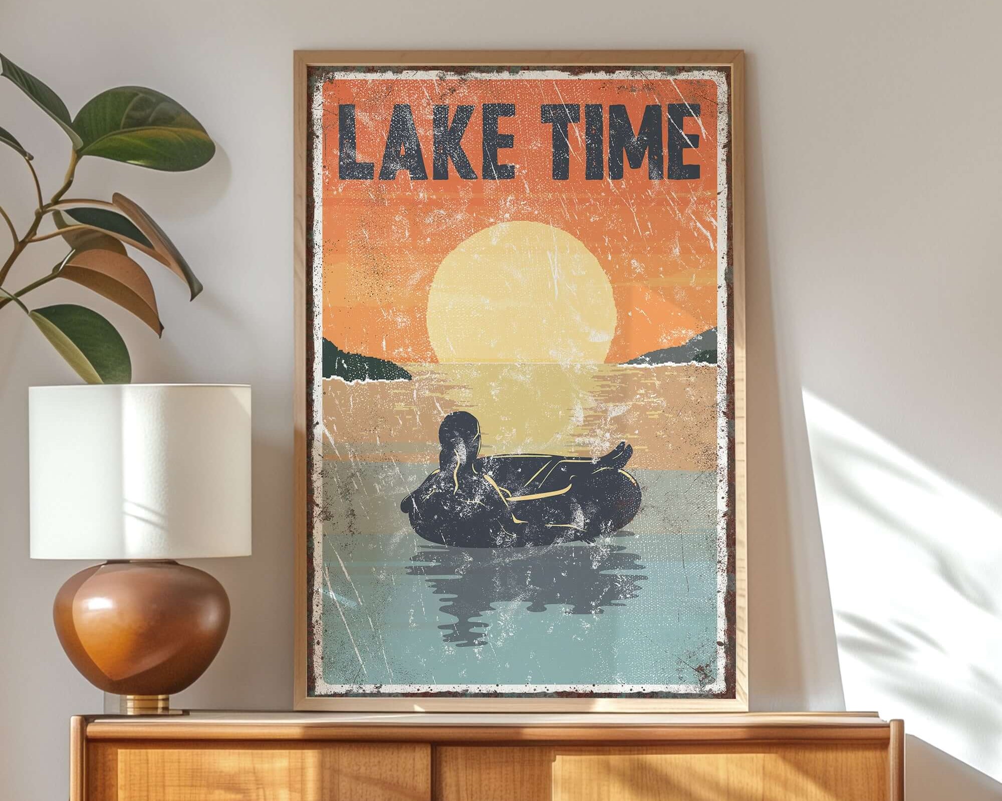 Display the "Lake Time Sunset Sign, Female Tubing"—a retro wall decor piece featuring a woman tubing at sunset—on a wooden sideboard with a lamp and plant to add modern farmhouse charm to your space.