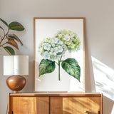 a wooden cabinet with a framed painting of a white hydrangea flower hanging on it. The painting is placed on a wooden shelf, and there is a lamp on the shelf as well.