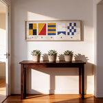 a wooden console table with three potted succulents on top, and a framed artwork with nautical flags hanging above it.