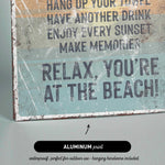 The image is a sign with text that reads "Relax, You're at the Beach!" and it is made of aluminum print.