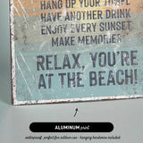 The image is a sign with text that reads "Relax, You're at the Beach!" and it is made of aluminum print.