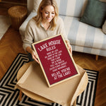 A woman is sitting on a couch and holding up a framed sign with a red background and white text.