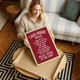 A woman is sitting on a couch and holding up a framed sign with a red background and white text.
