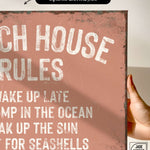 a hand holding a sign that says beach house rules