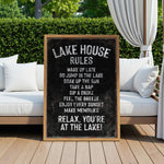 A black and white sign with white text is displayed in front of a wooden deck with white cushions and a white curtain.