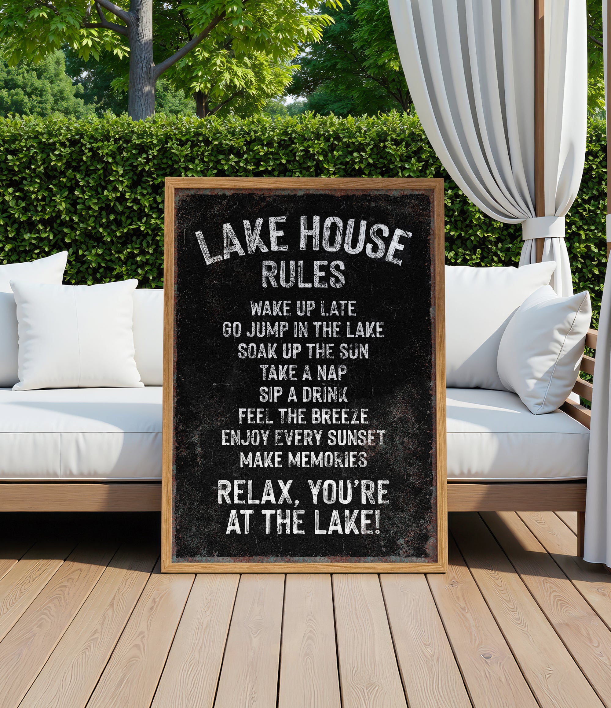 A black and white sign with white text is displayed in front of a wooden deck with white cushions and a white curtain.